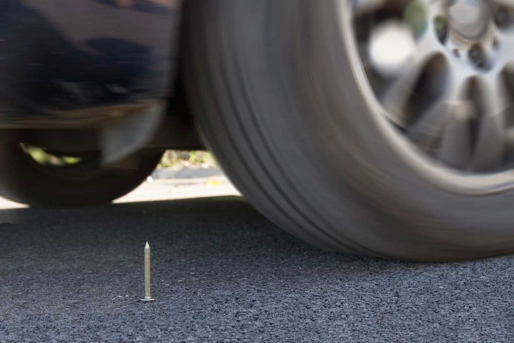 Car tire about to catch a nail on the road
