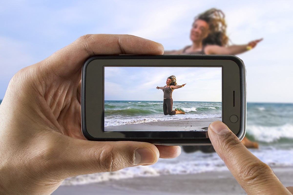 Man taking a picture of a woman jumping on the beach